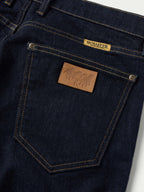 Dark rinse denim pocket close-up with logo patch and rivets