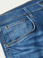 Medium-wash denim dungaree jeans close-up of front pocket flap and metal buttons