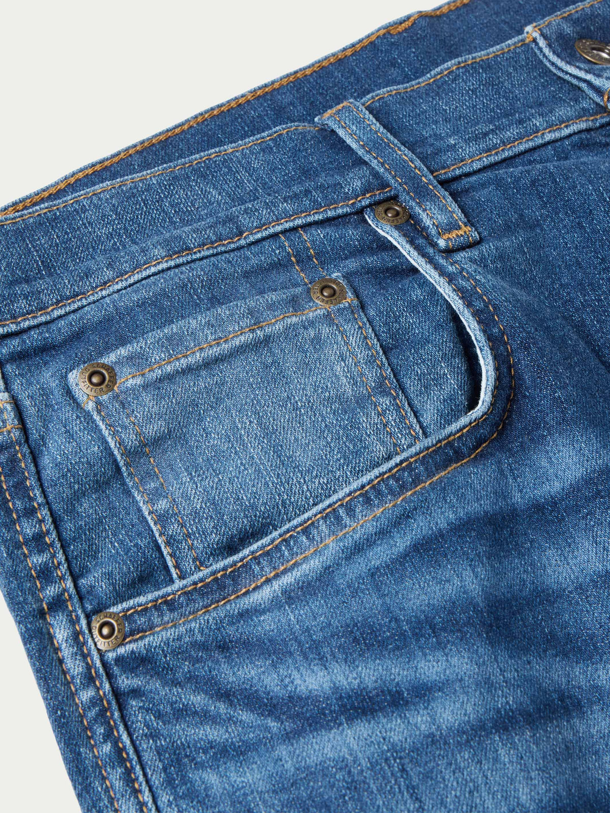 Medium-wash denim dungaree jeans close-up of front pocket flap and metal buttons