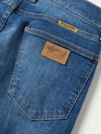 Medium-wash dungaree jeans close-up of back pocket with leather brand patch