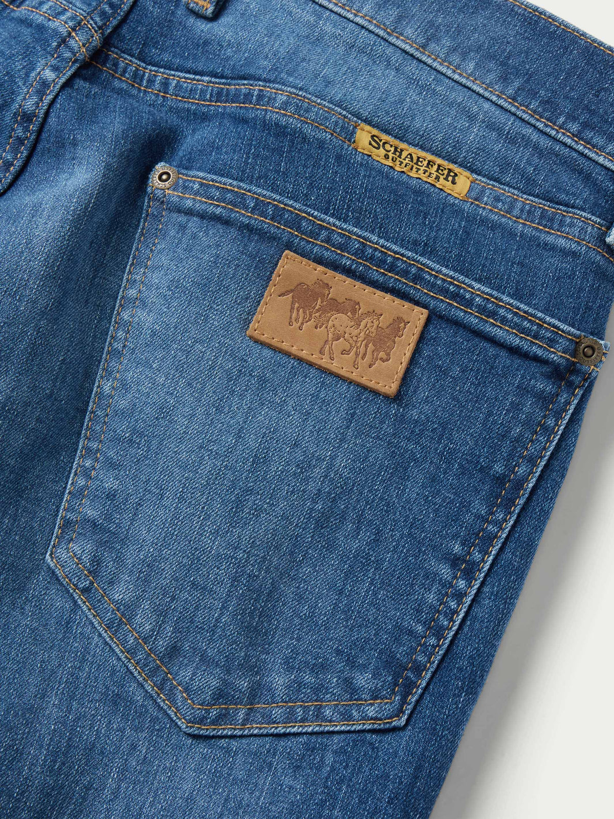 Medium-wash dungaree jeans close-up of back pocket with leather brand patch
