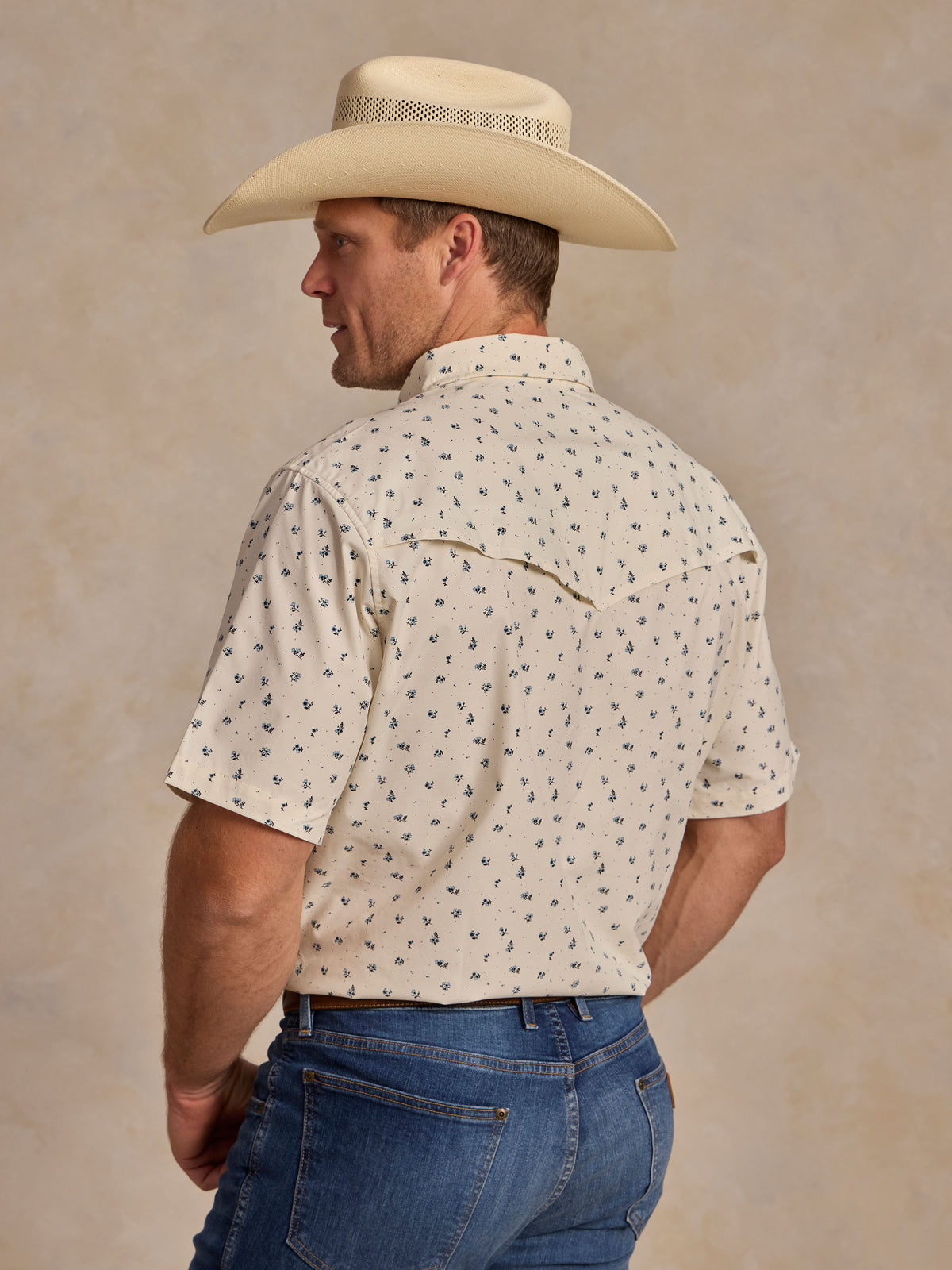 Short-sleeve pearl snap shirt on model, back view: white with small blue floral pattern.