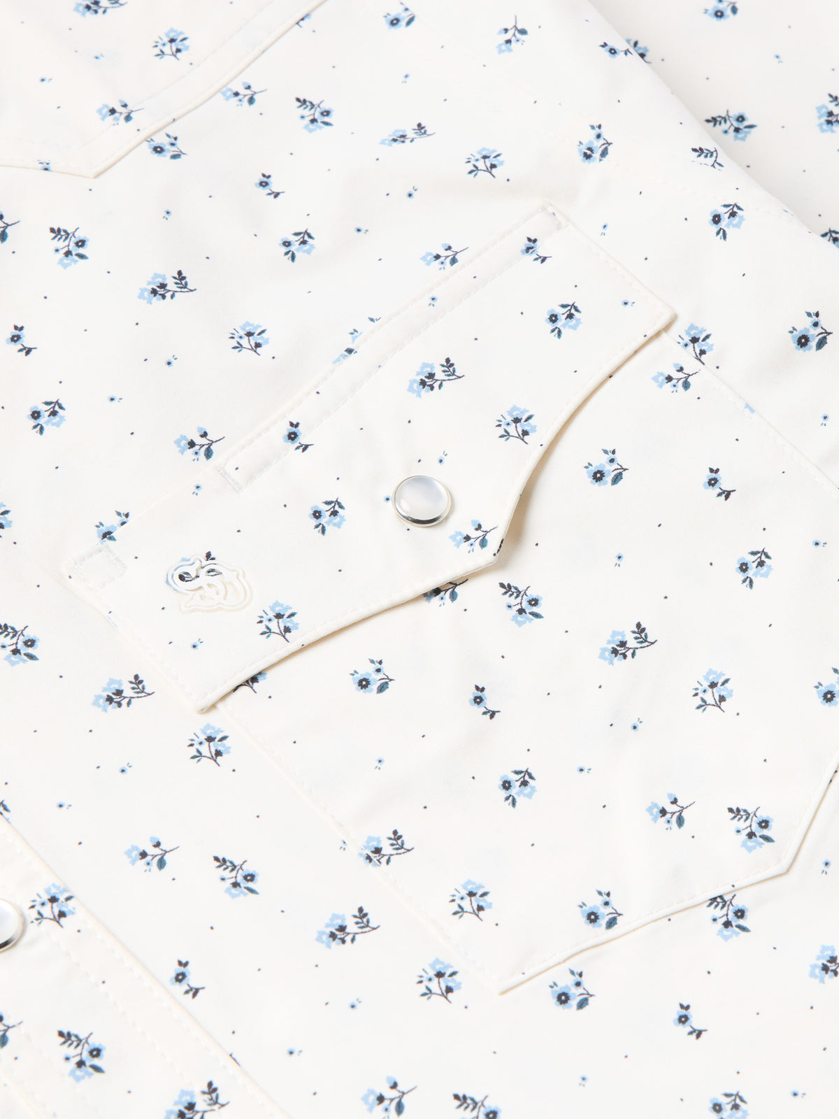 Short-sleeve pearl snap shirt detail: white fabric, blue floral print, round snap buttons.