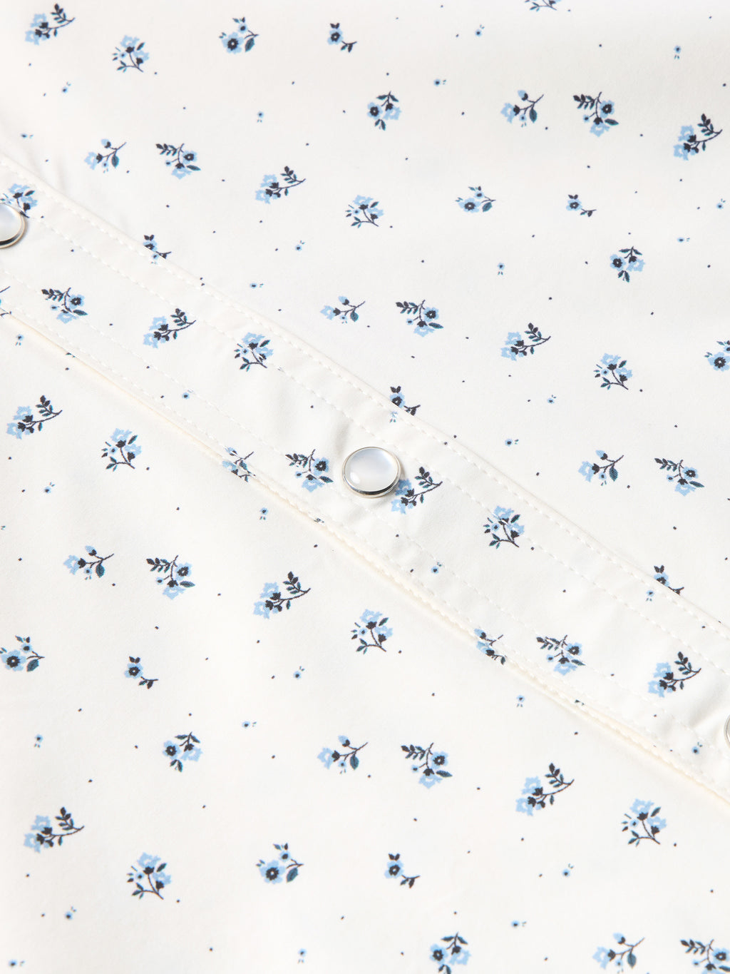 Short-sleeve pearl snap shirt fabric detail in white with small blue floral print and snap.