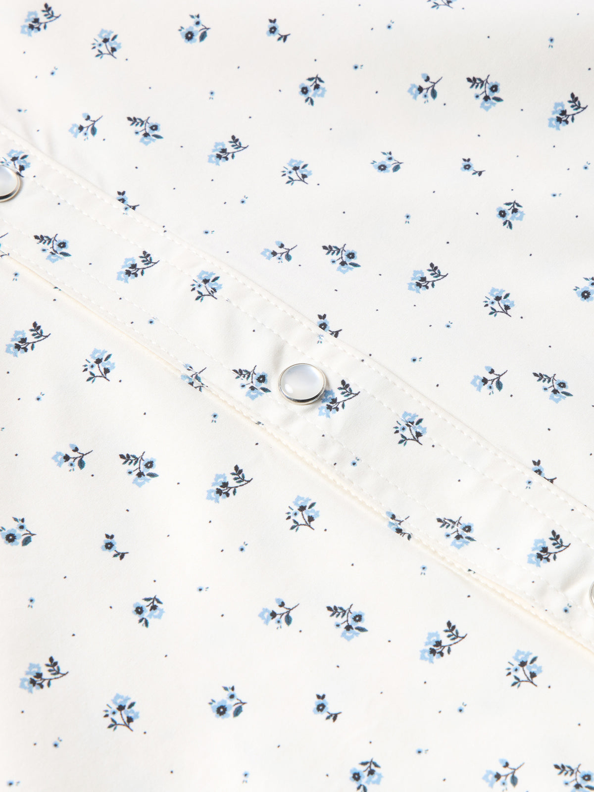 Short-sleeve pearl snap shirt fabric detail in white with small blue floral print and snap.