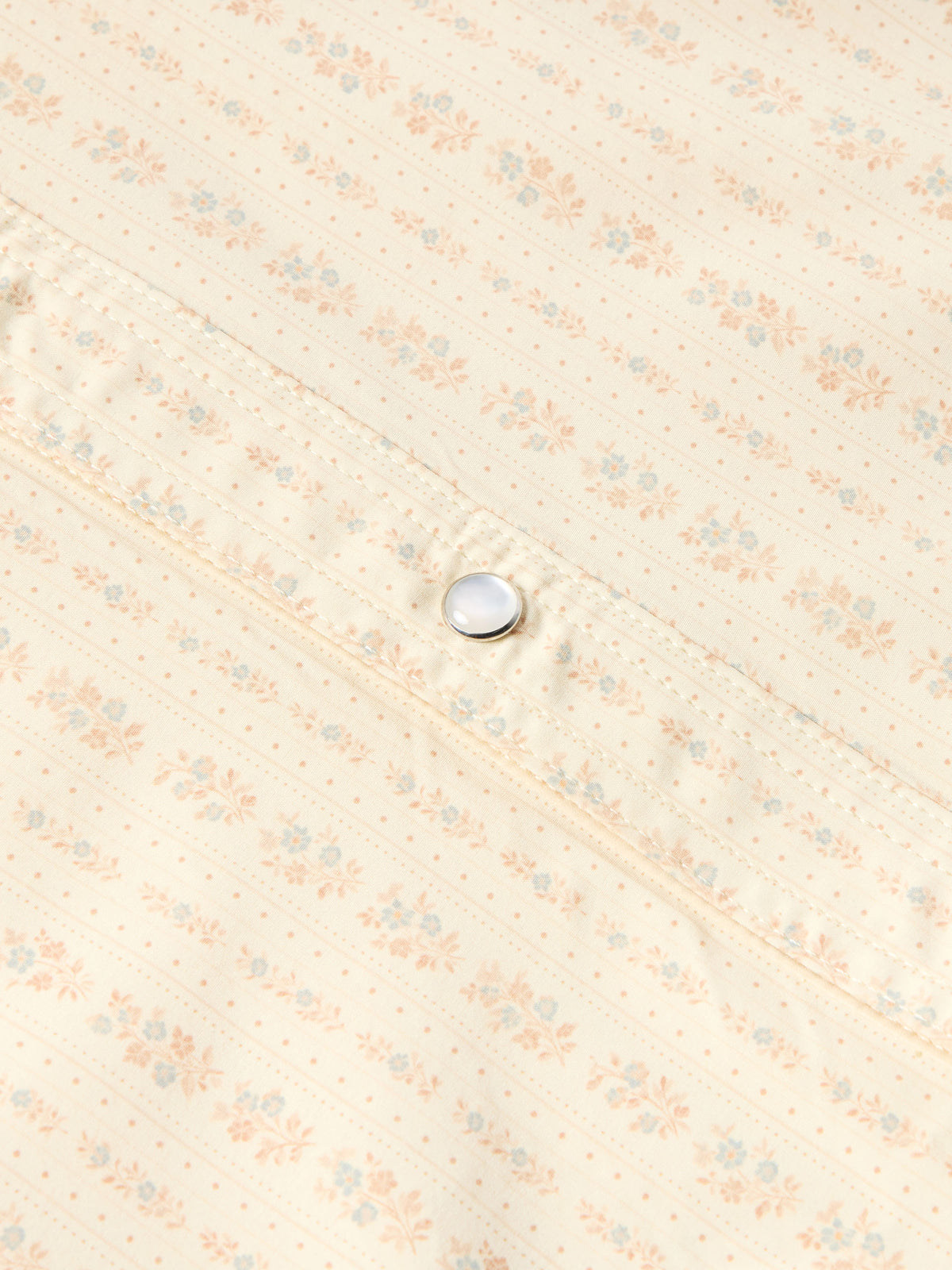Close-up of round pearl snap button on light cream patterned western shirt.