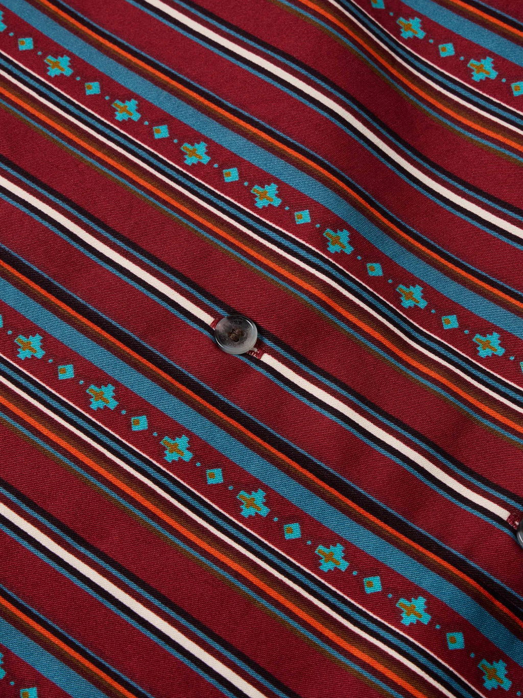 Detail of red striped button-down fabric with teal star-like motifs and white bands