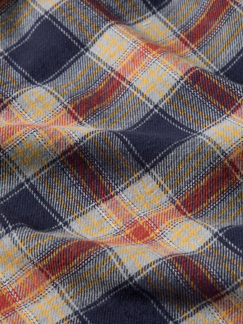 Multicolor flannel plaid fabric close-up with navy, orange, and cream grid lines.