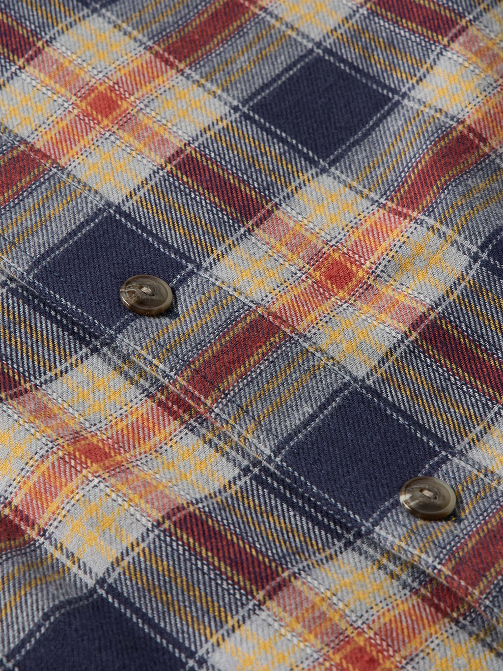 Flannel plaid fabric close-up with button at chest pocket and layered weave texture.