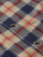 Flannel plaid fabric close-up with button at chest pocket and layered weave texture.