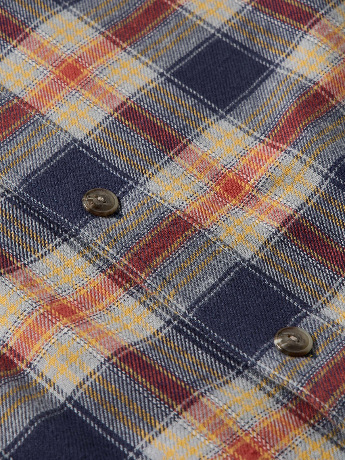 Flannel plaid fabric close-up with button at chest pocket and layered weave texture.