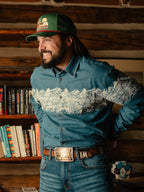 Man wearing light blue denim button-down shirt with white mountain print across chest