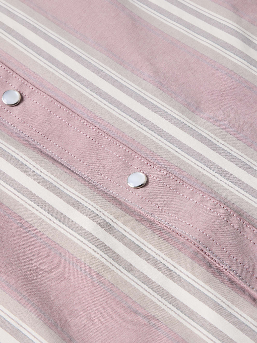 Pink striped shirt fabric close-up with rows of stitching and metal buttons