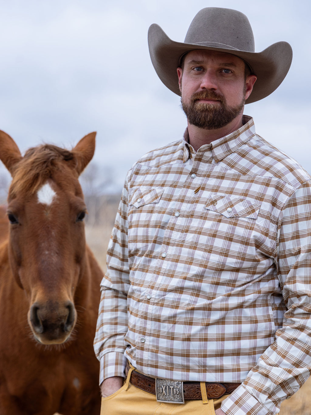 Western snap shirt on a cowboy hat model in tan-and-white plaid; horse beside him.