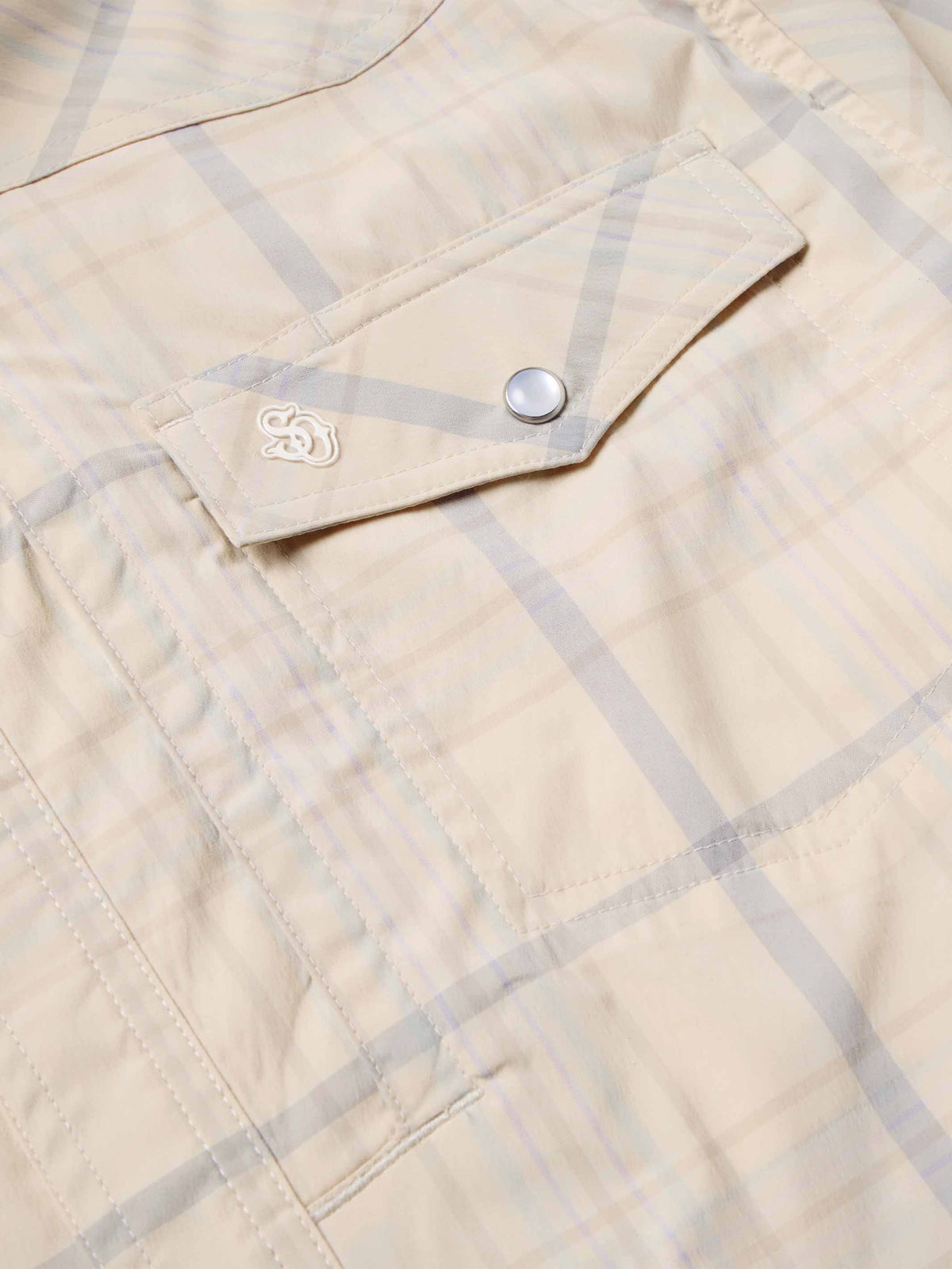 Snap shirt chest pocket detail, cream with blue plaid, snap flap and embroidered emblem.