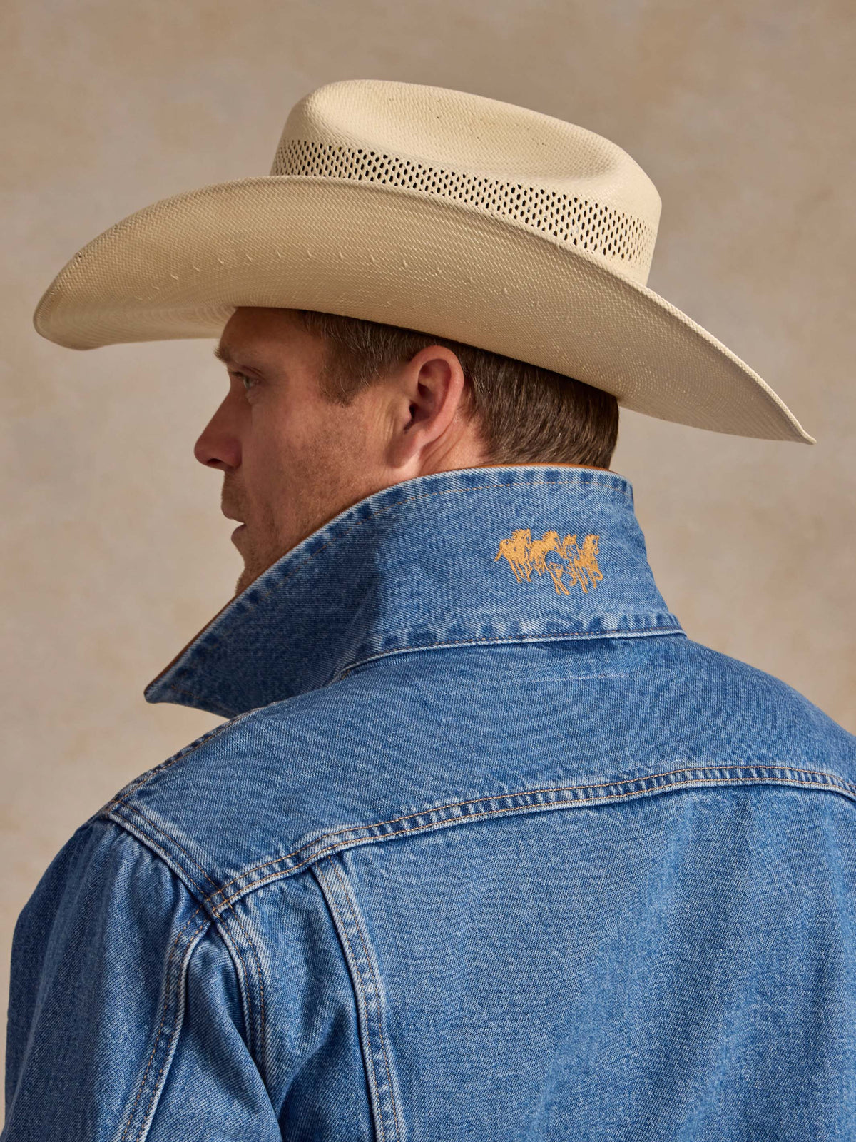 Medium indigo denim jacket showing back yoke with small yellow/orange embroidered patch