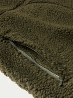 Olive fleece jacket close-up showing front zipper and textured fabric surface.