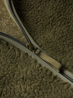 Olive zipper close-up with metal pull and stitched zipper tape on fleece jacket.