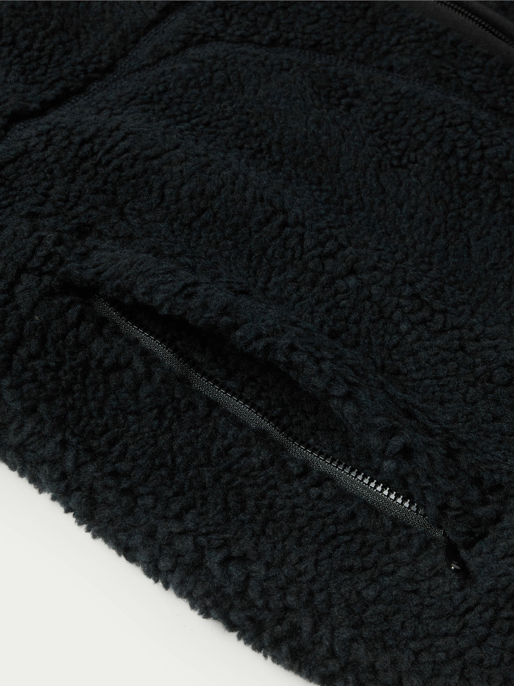 Black fleece jacket corner with zipper track and textured fabric.