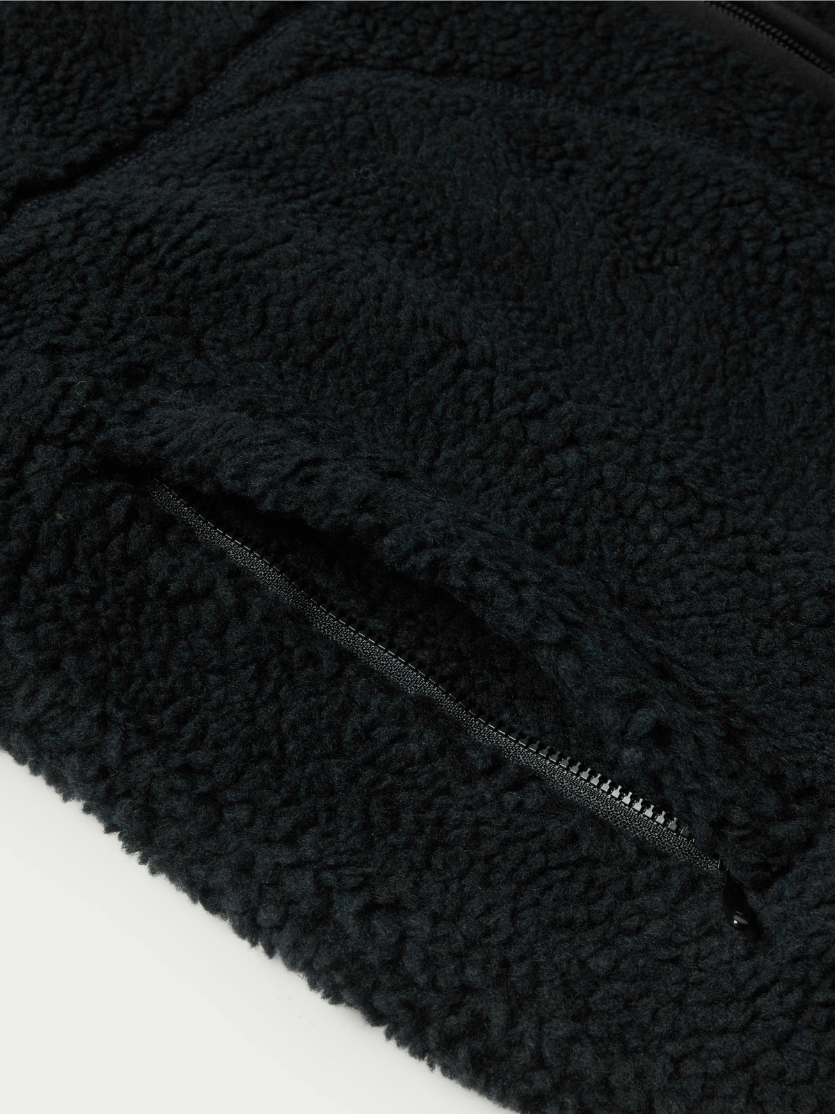 Black fleece jacket corner with zipper track and textured fabric.