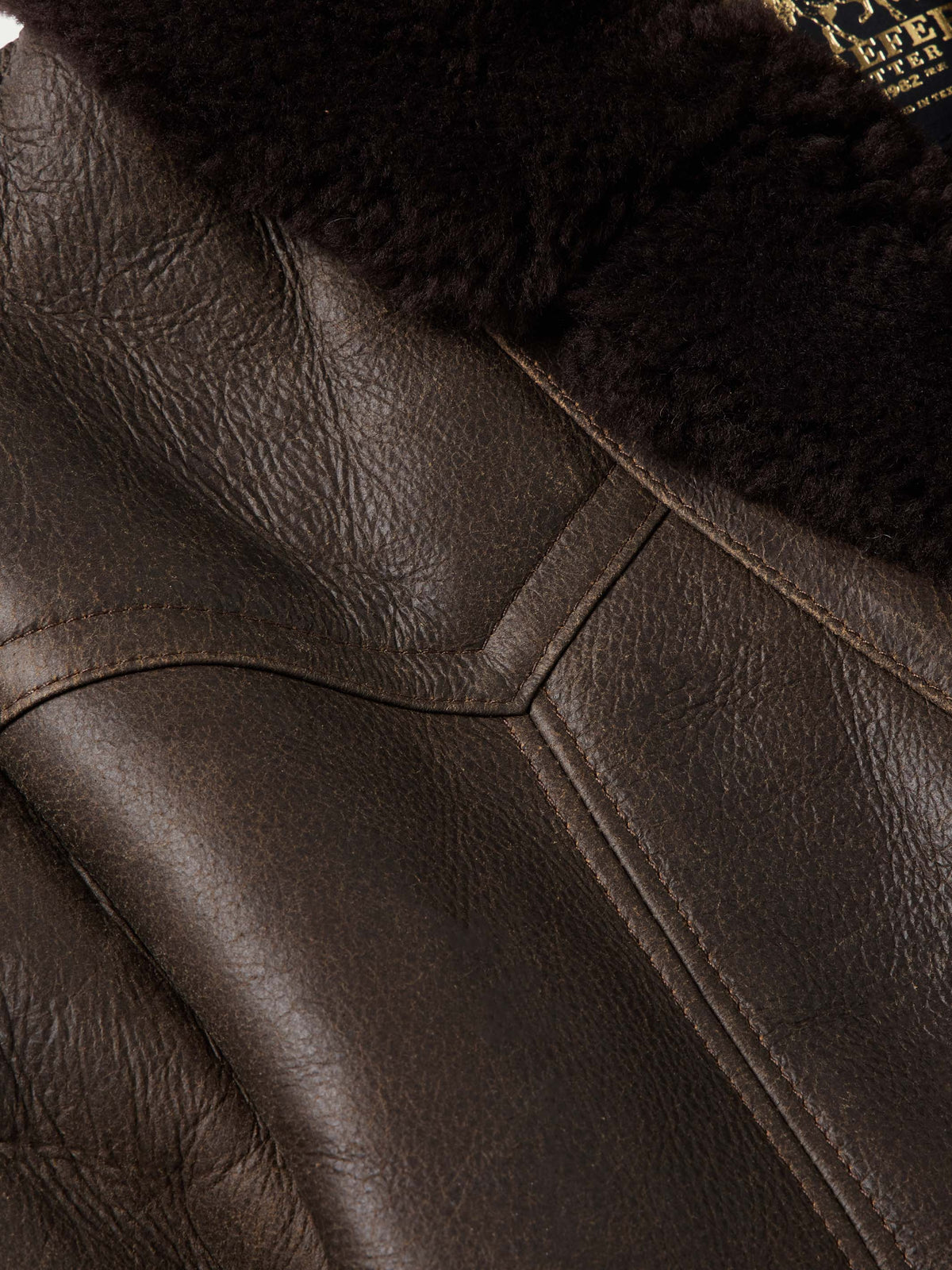 Leather coat shoulder and seam stitching detail in dark brown