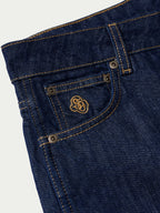 Dark denim jeans close-up of front pocket with contrast stitch and metal button