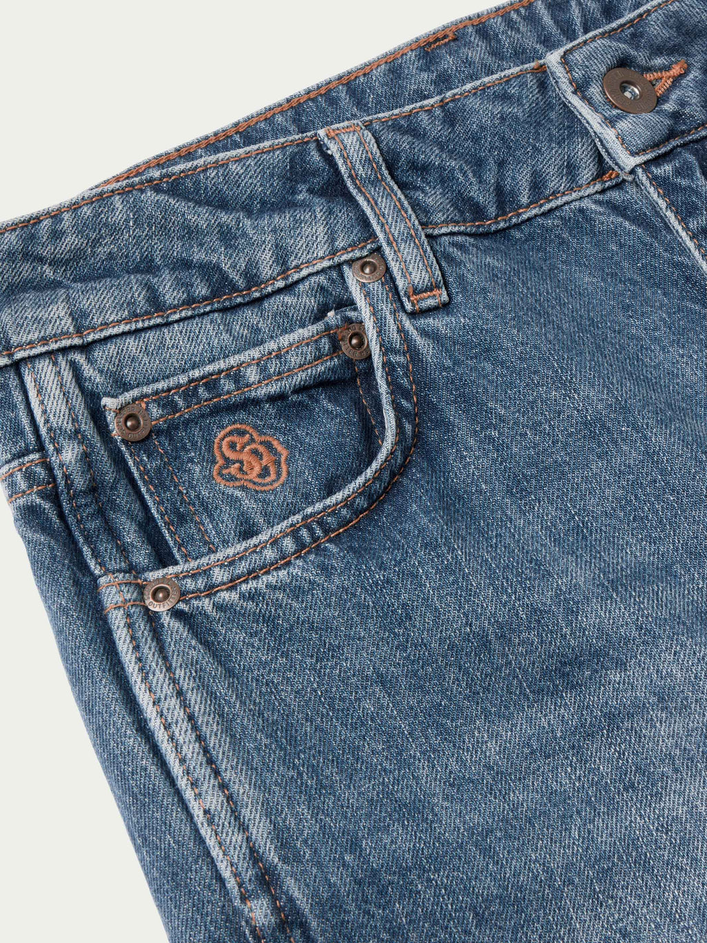Medium-wash denim waistband close-up with stud buttons and stitched logo patch.