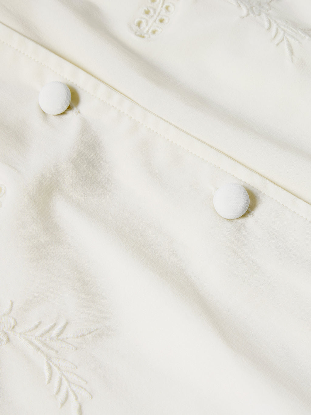 Cream blouse front with decorative embroidery and fabric-covered button closures