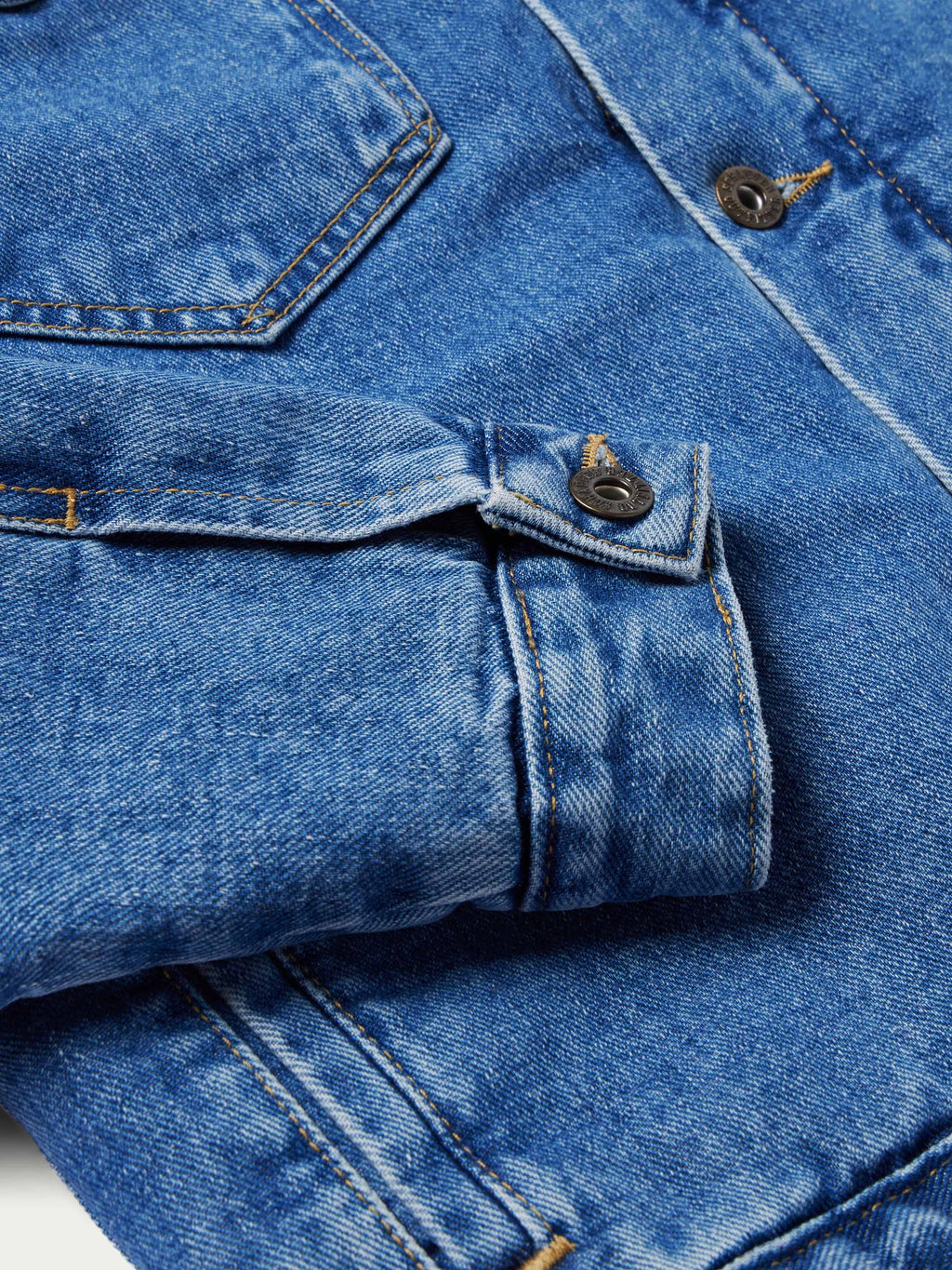 Indigo denim jacket cuff with adjustable button strap and metal hardware