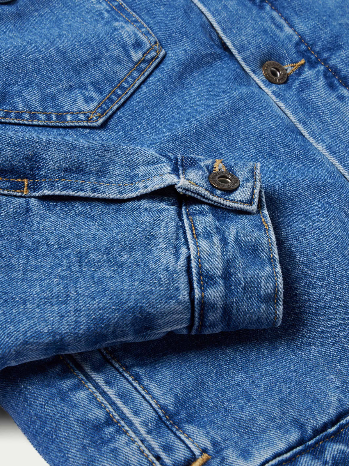 Indigo denim jacket cuff with adjustable button strap and metal hardware