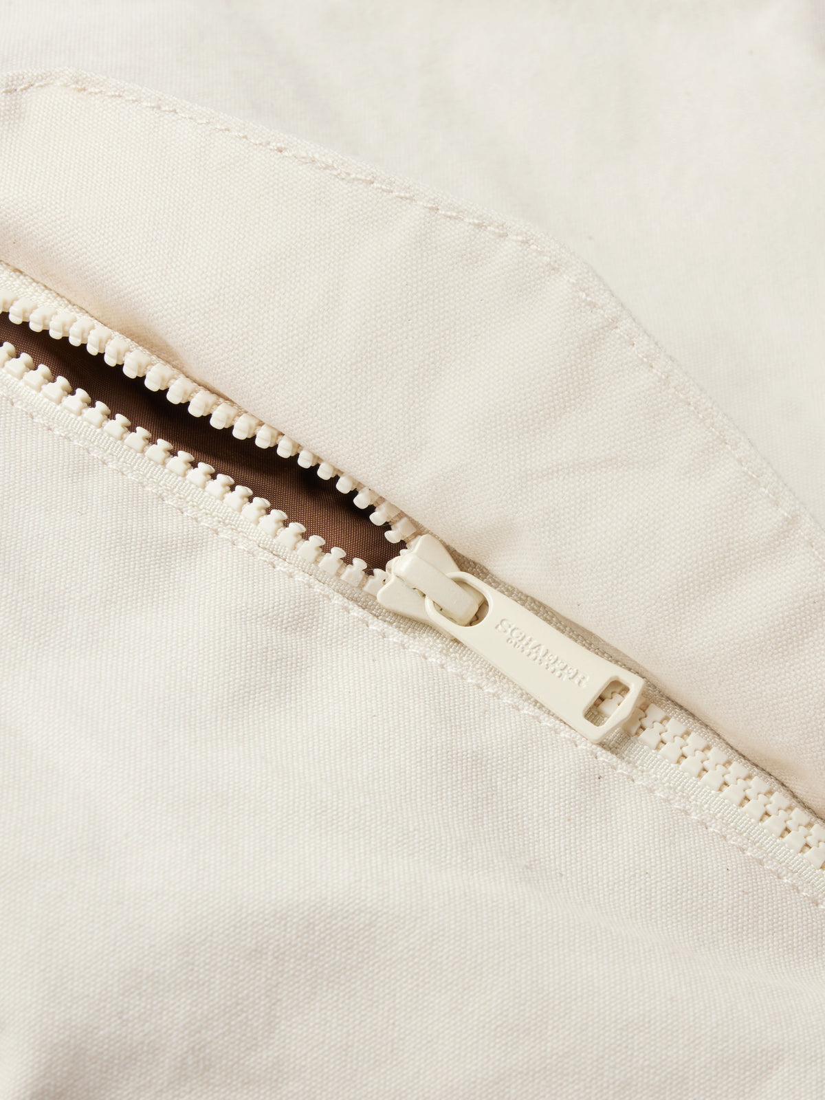 Natural canvas coat zipper detail with white stitching and snap placket
