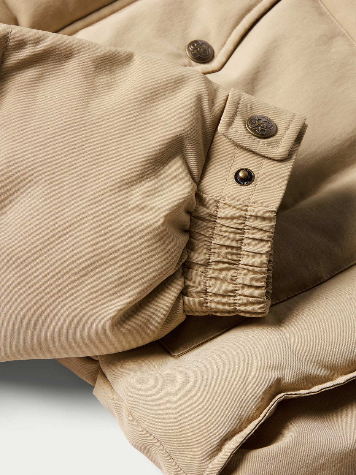 Tan and cream down jacket sleeve cuff close-up with ruched elastic and snaps