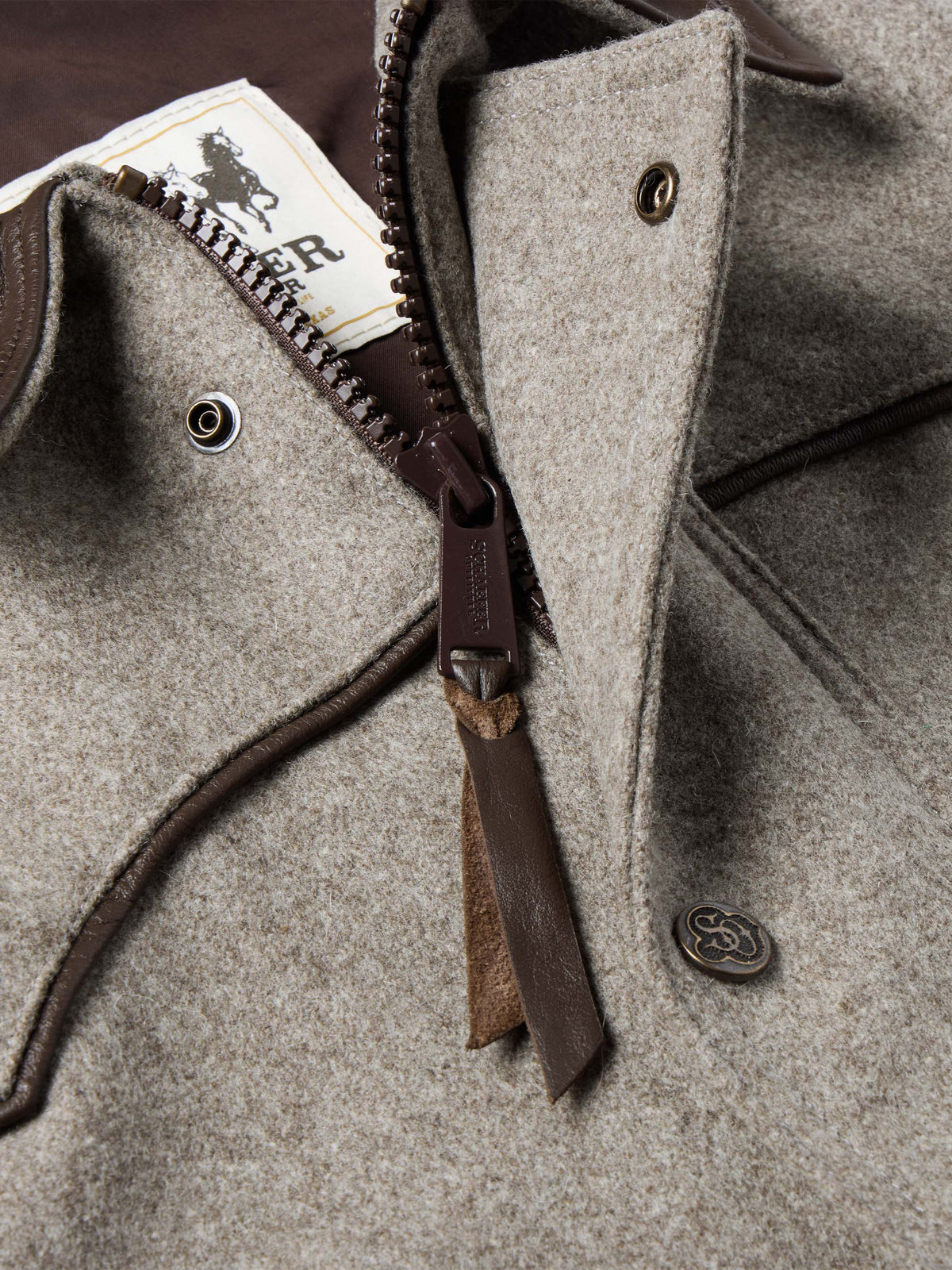 Taupe wool vest close-up showing dark zipper pull, snap buttons, and leather trim