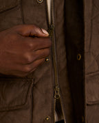 Brown quilted microsuede jacket detail: hand on brass zip and snap placket
