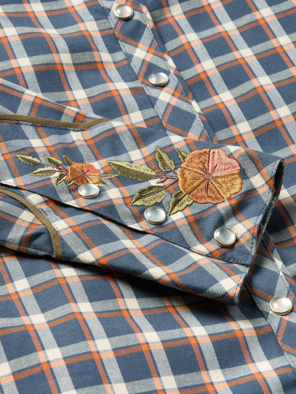 Women’s embroidered snap shirt close-up, blue plaid with floral embroidery and snap buttons