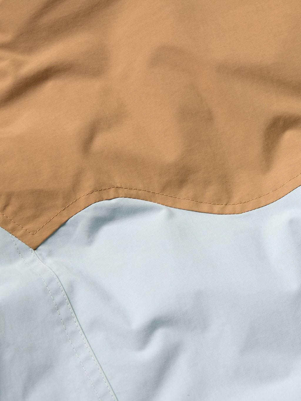 Women’s down jacket close-up of tan and light blue color-block seam detail