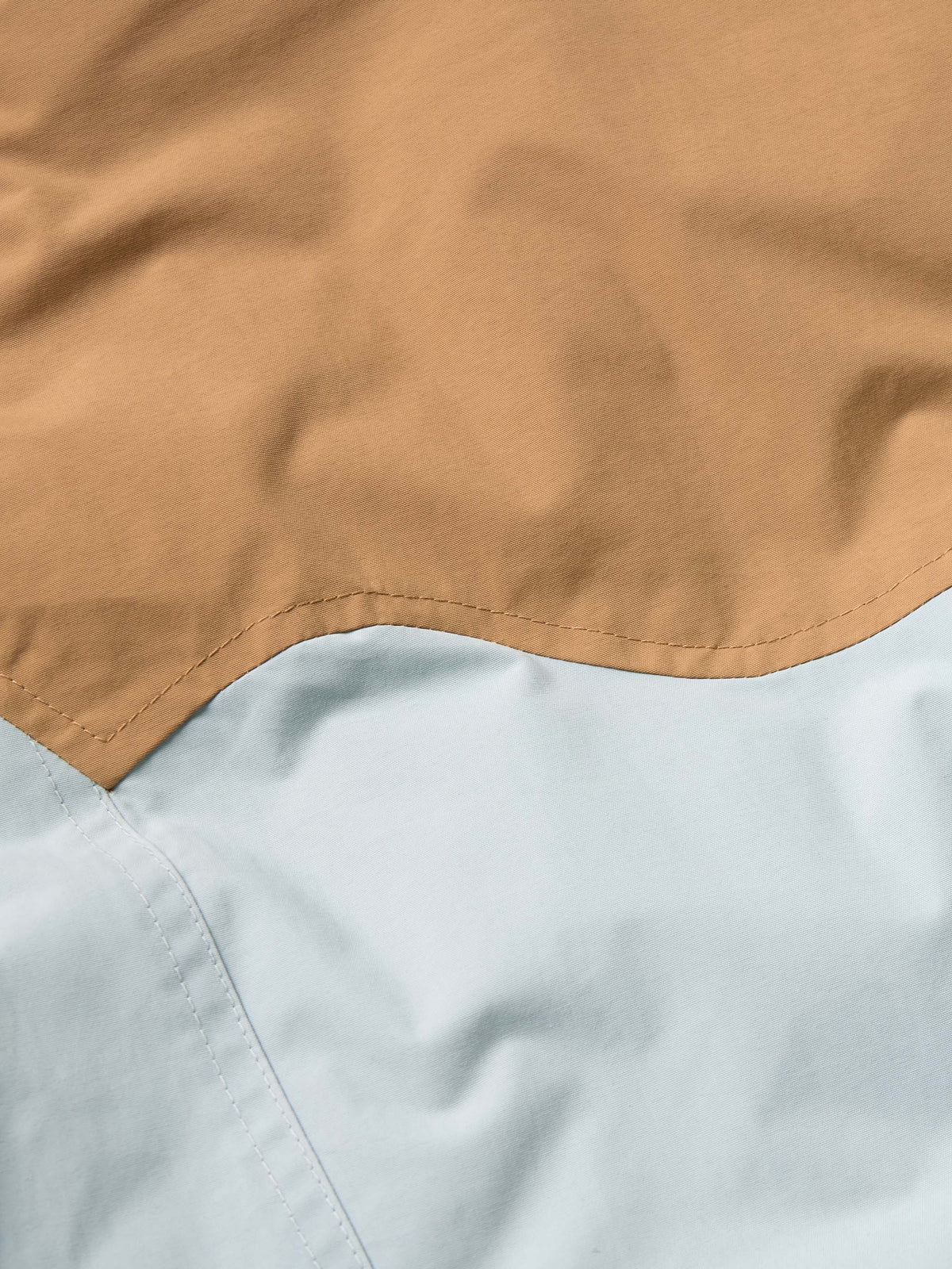 Women’s down jacket close-up of tan and light blue color-block seam detail