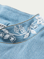 Light wash denim jacket neckline with white floral embroidery and bead accents