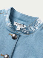 Light wash denim jacket with four snap buttons and white embroidered yoke trim