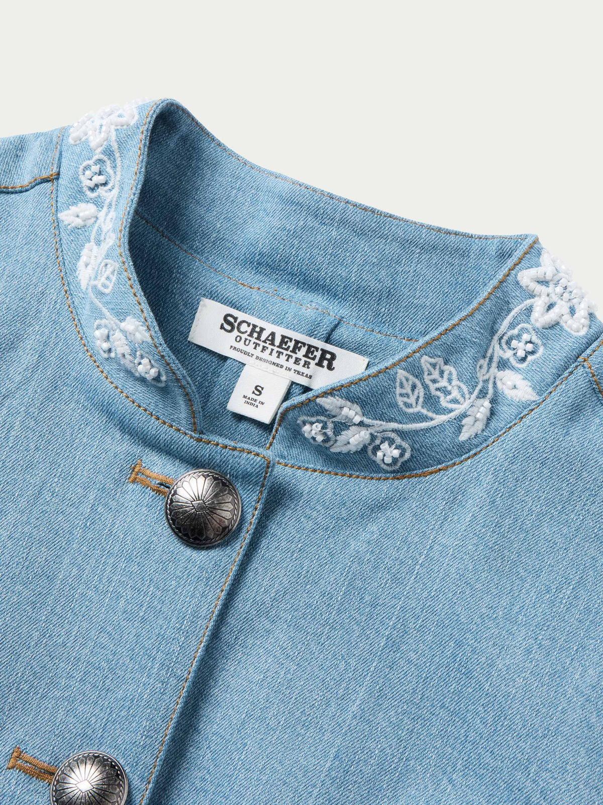 Light wash denim jacket with four snap buttons and white embroidered yoke trim