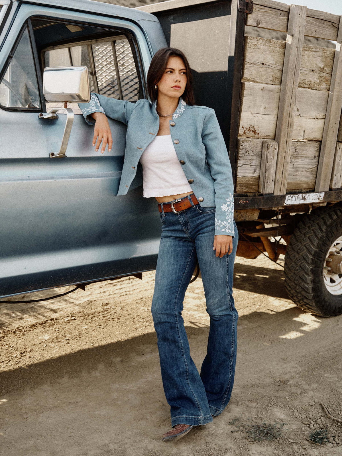 Light wash denim jacket with snap front, white embroidered cuffs, and dark jeans