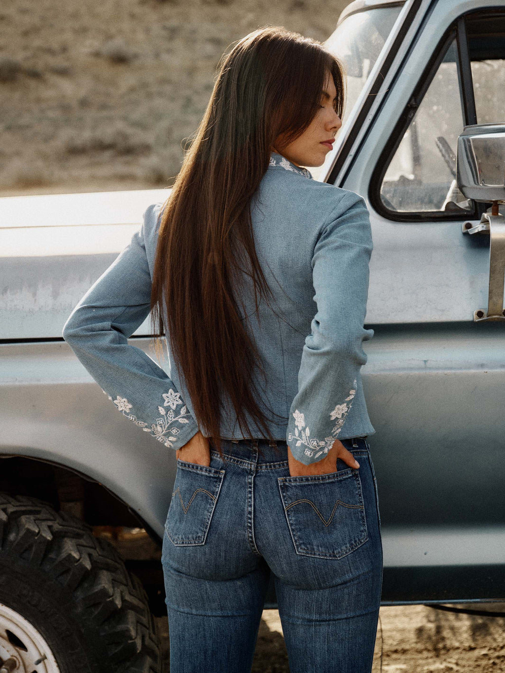 Light wash denim jacket on model with white embroidered back cuff details