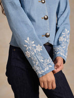 Light wash denim jacket sleeve close-up with white embroidered floral trim