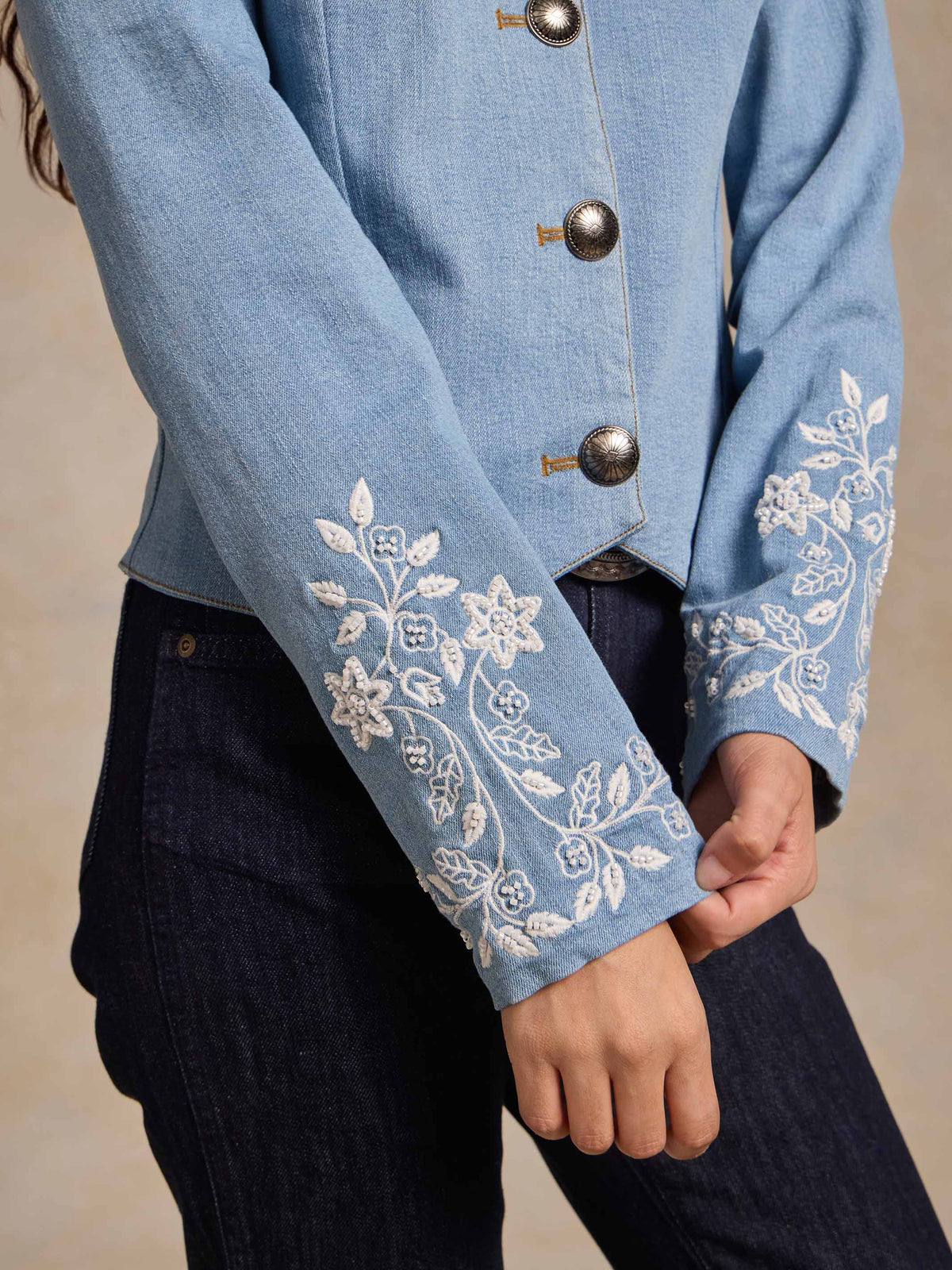 Light wash denim jacket sleeve close-up with white embroidered floral trim