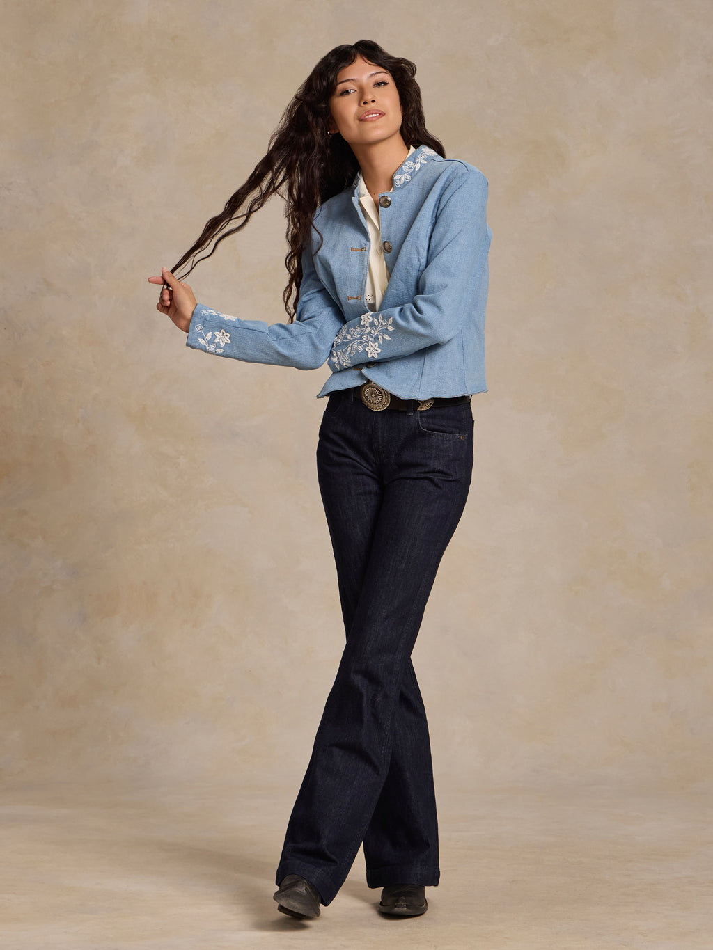 Light wash denim jacket on model with embroidered sleeves and button front, cropped hem