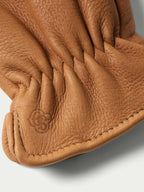 Saddle deerskin glove thumb and cuff stitching with embossed logo