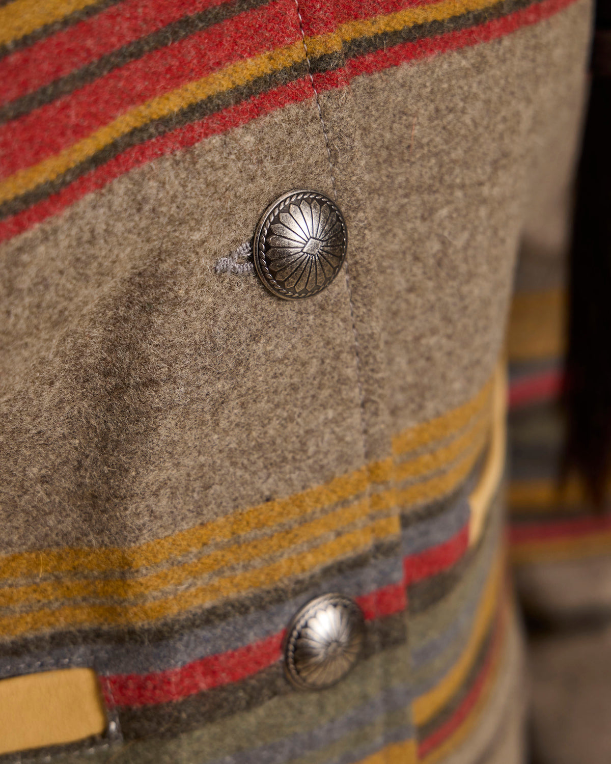 Close-up of jacket button and striped fabric panel on taupe wool