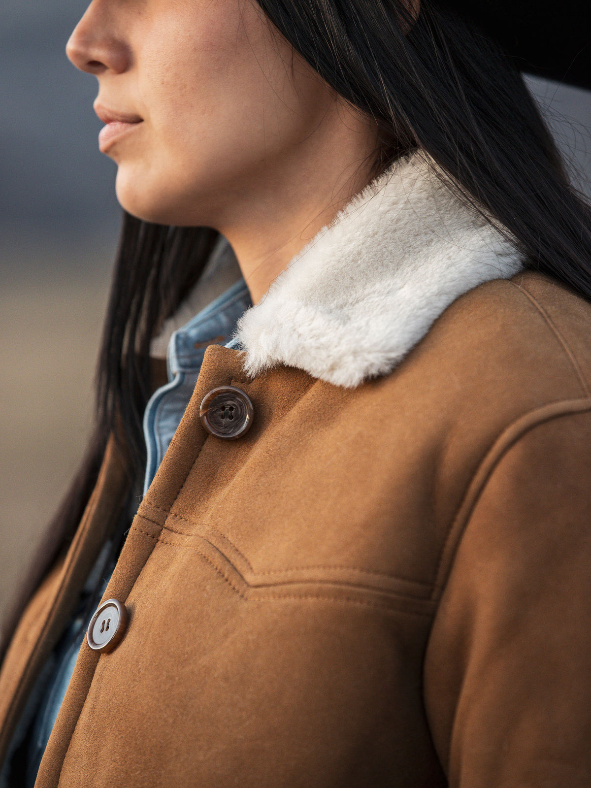 Close-up of brown shearling jacket shoulder with tan sherpa collar and button