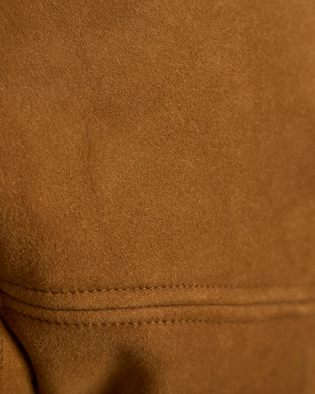 Brown shearling jacket fabric close-up with curved seam at hemline