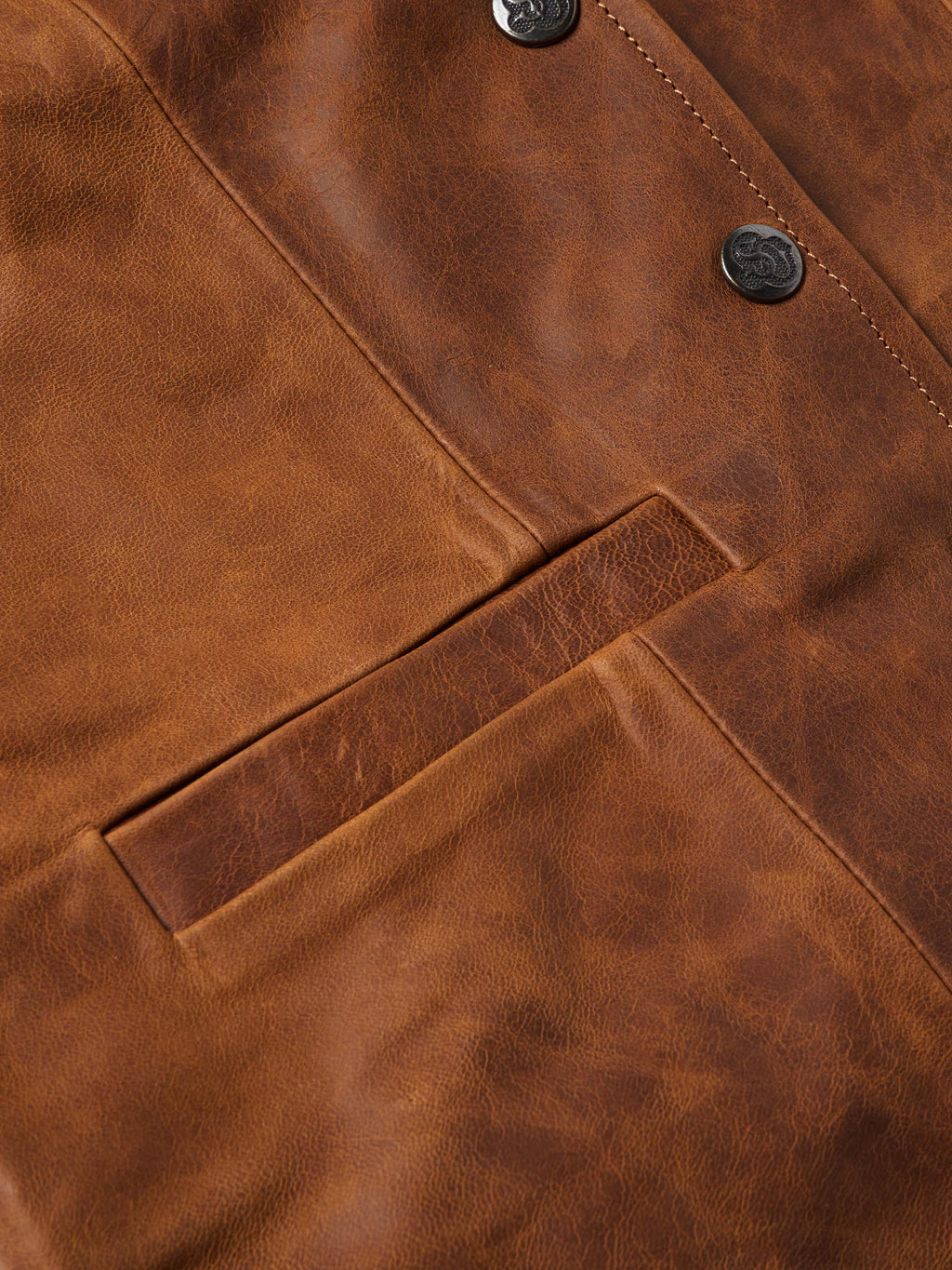 Close-up of whiskey-brown leather vest chest pocket, buttons, and stitching